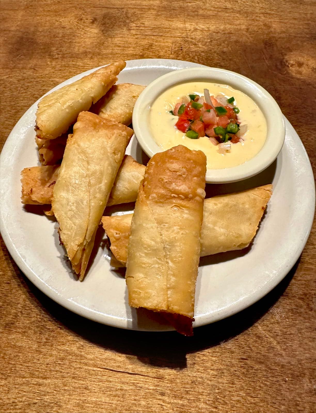 Golden fried crispitos on a plate with a side of melted queso topped with fresh pico de gallo.